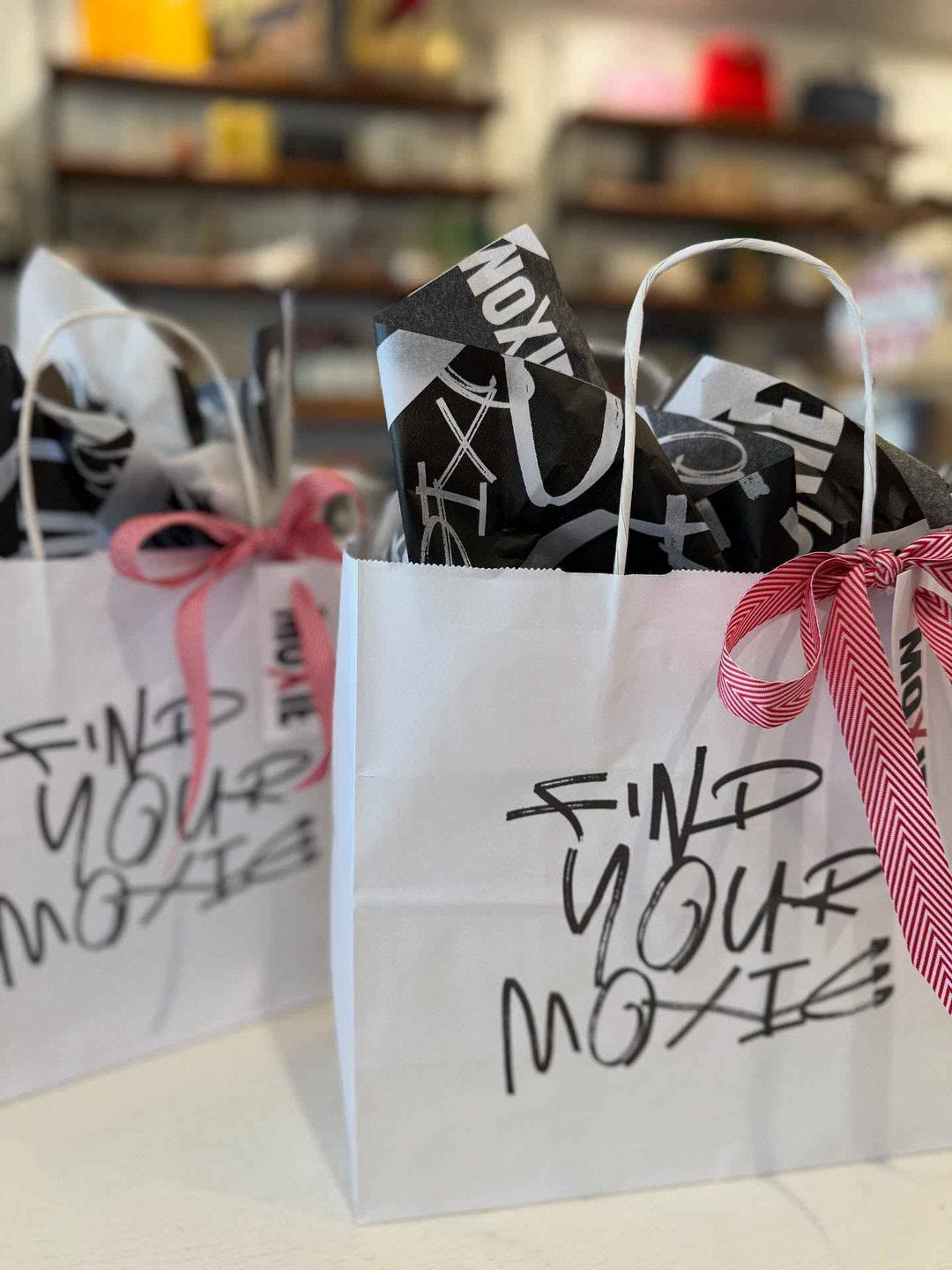 White gift bag with 'Find Your Moxie' text, filled with black and white tissue
