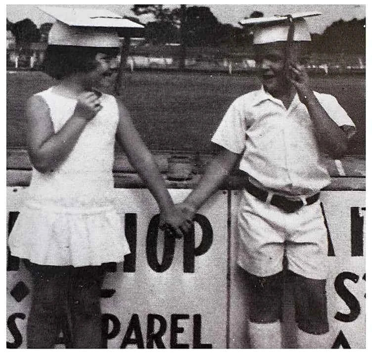 Two childreb in vintage attire standing next to a sign with text.